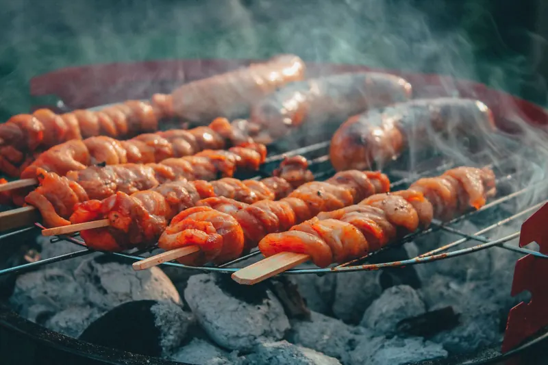 Delicious meat skewers and sausages grilling over a charcoal barbecue, emitting rich smoke and flavors