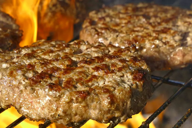 Close-up of juicy beef burgers grilling over open flames, perfect for summer BBQs