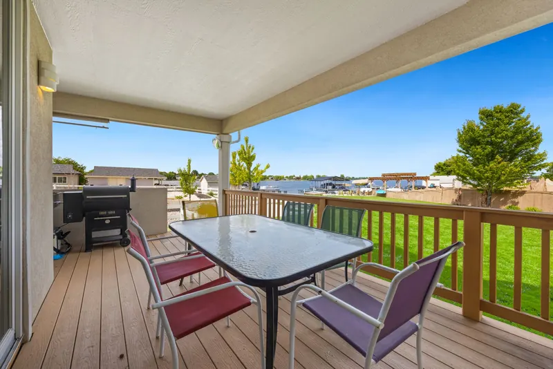 Spacious patio with outdoor seating and BBQ overlooking a serene lake on a sunny day