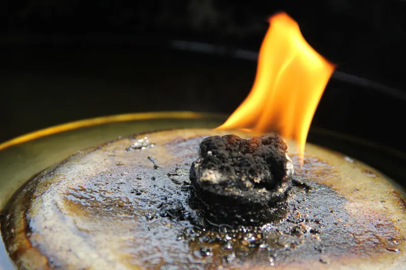 A vibrant flame ignites a piece of charcoal in an artistic close-up shot
