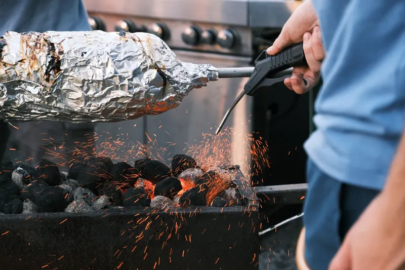 Barbecue cooking with foil-wrapped food over charcoal flames showing flying sparks and intense heat