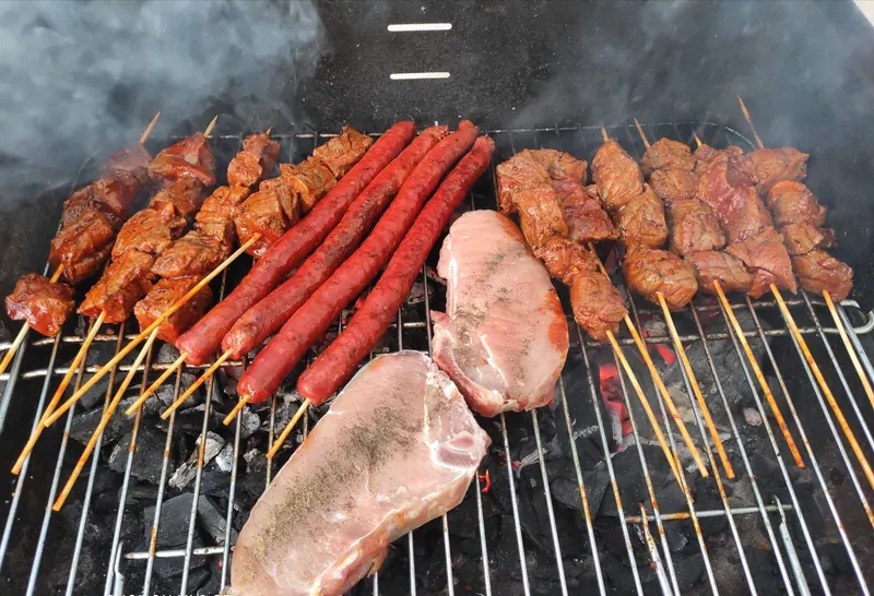 A variety of meats being grilled on a charcoal barbecue