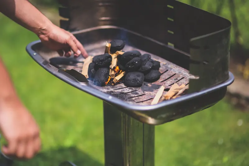 Hand preparing charcoal briquettes for grilling outdoors in summer