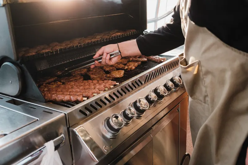 Person wearing apron grilling meat on a barbecue. Outdoor cooking scene