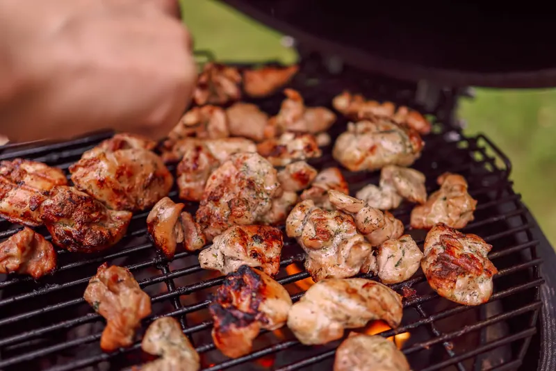 Sizzling chunks of grilled chicken cooking on an outdoor barbecue with charcoal flames