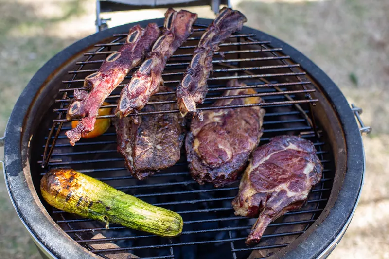 Close-up of assorted meats and zucchini grilling outdoors in daylight