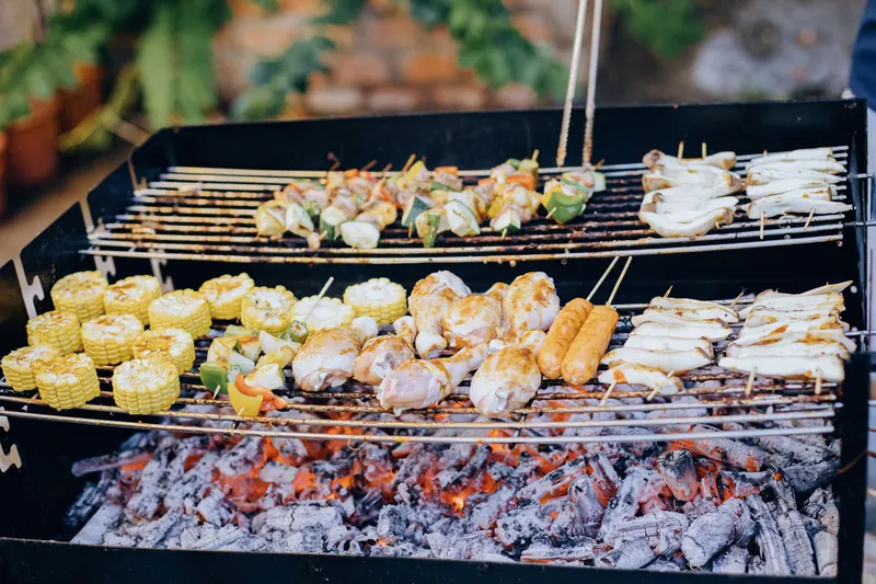 A variety of foods grilling over hot coals in an outdoor barbecue setup
