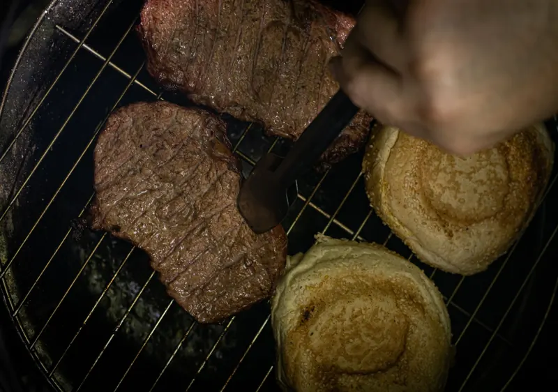 Close-up of juicy meat and buns grilling outdoors with tongs