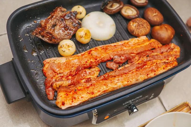 Close-up of pork belly and vegetables grilling on an electric pan for a delicious meal