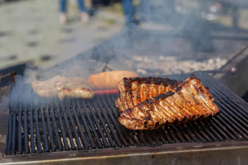 Grilling smoky ribs and sausages on an outdoor barbecue with visible smoke